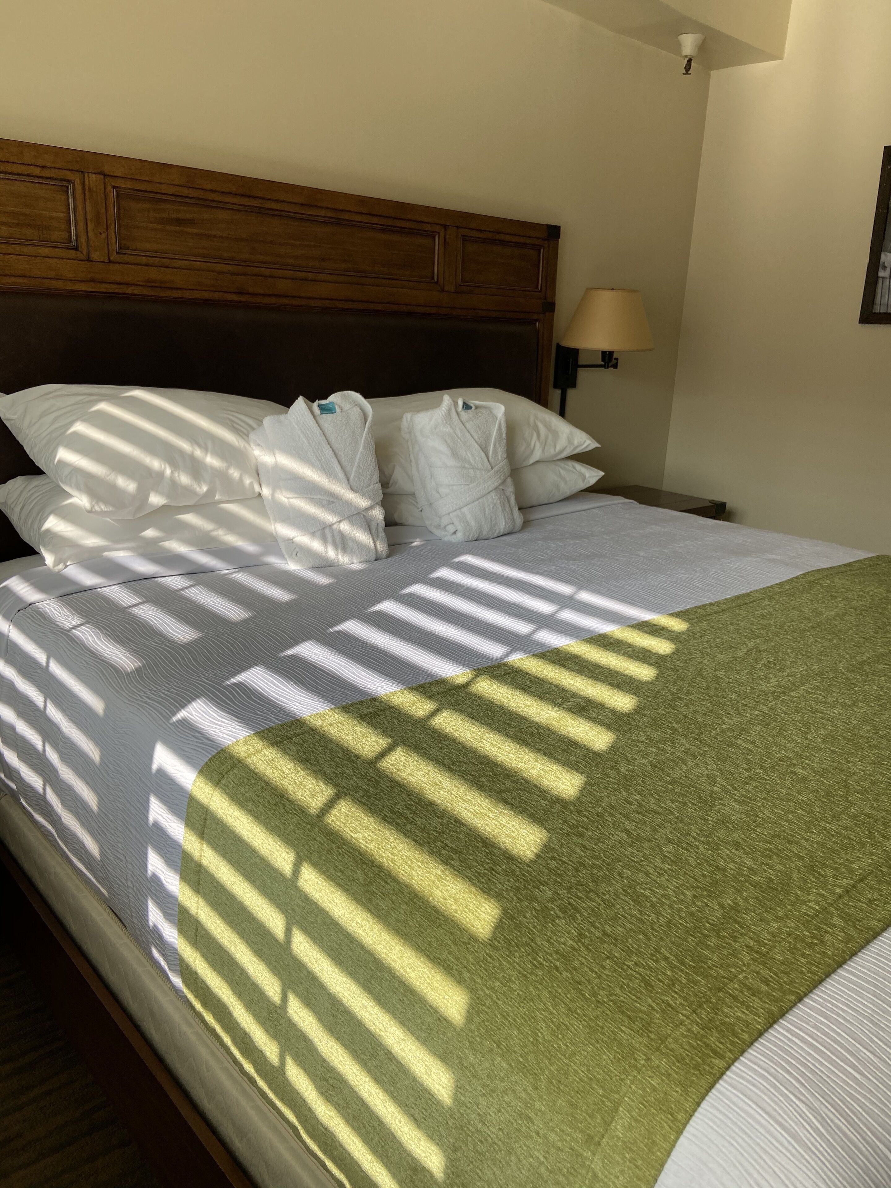 A neatly made bed with white bedding and a green throw blanket, a wooden headboard, and a bedside lamp.