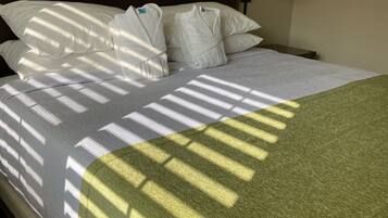 A neatly made bed with white bedding and a green throw blanket, a wooden headboard, and a bedside lamp.