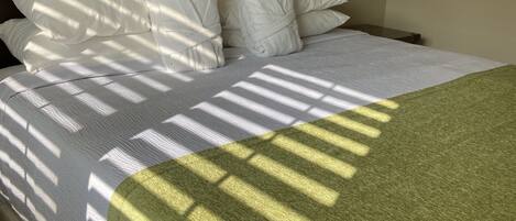 A neatly made bed with white bedding and a green throw blanket, a wooden headboard, and a bedside lamp.