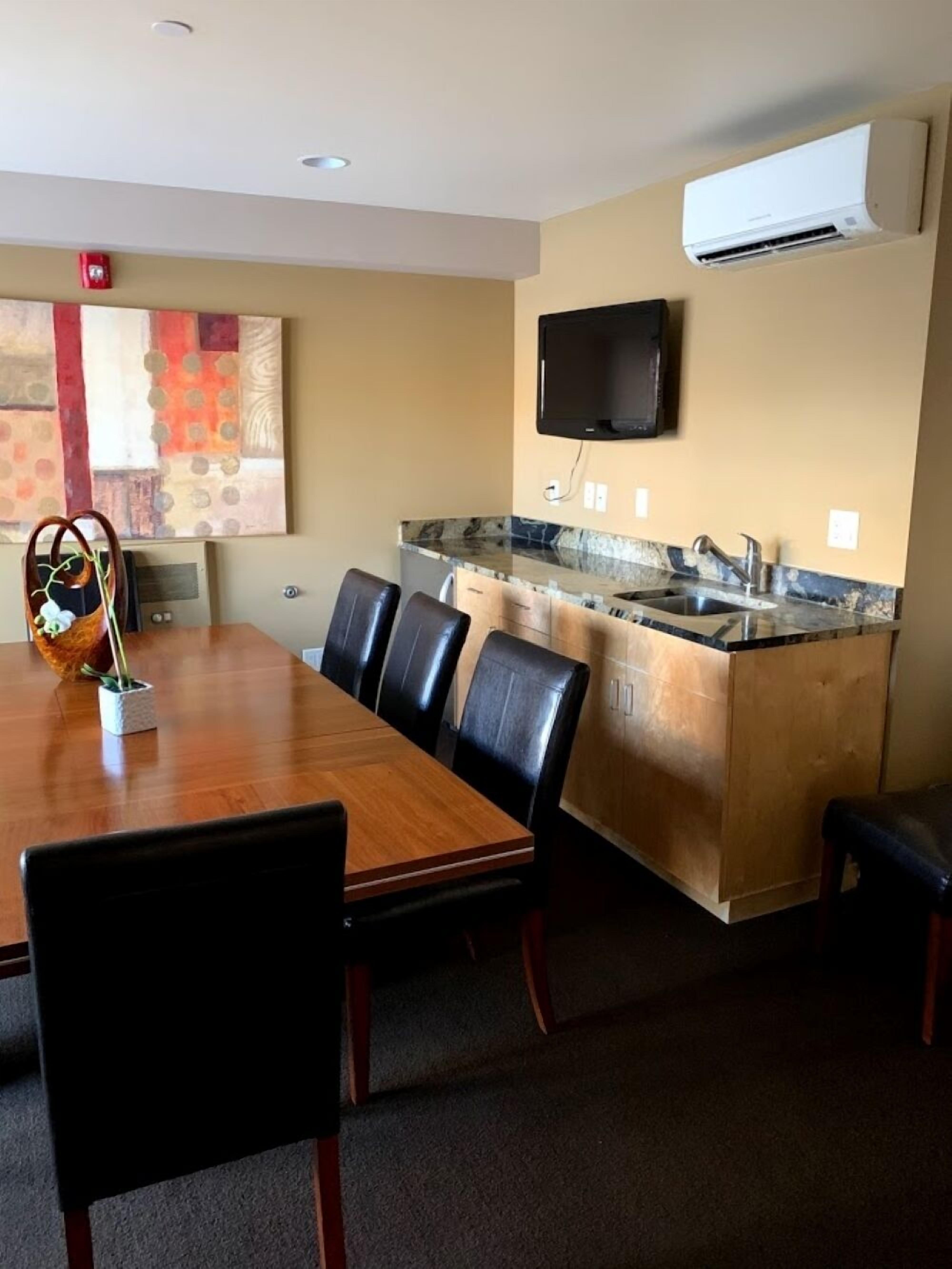 A modern kitchen with a built-in island, a flat-screen TV, and a dining area with a wooden table and leather chairs.