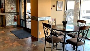 A dining area with a round table and four chairs, a fire extinguisher, and a view of the outside through a glass door.