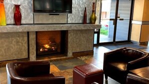 A modern lounge area with a flat-screen TV, a fireplace, leather sofas, and a patterned wall.