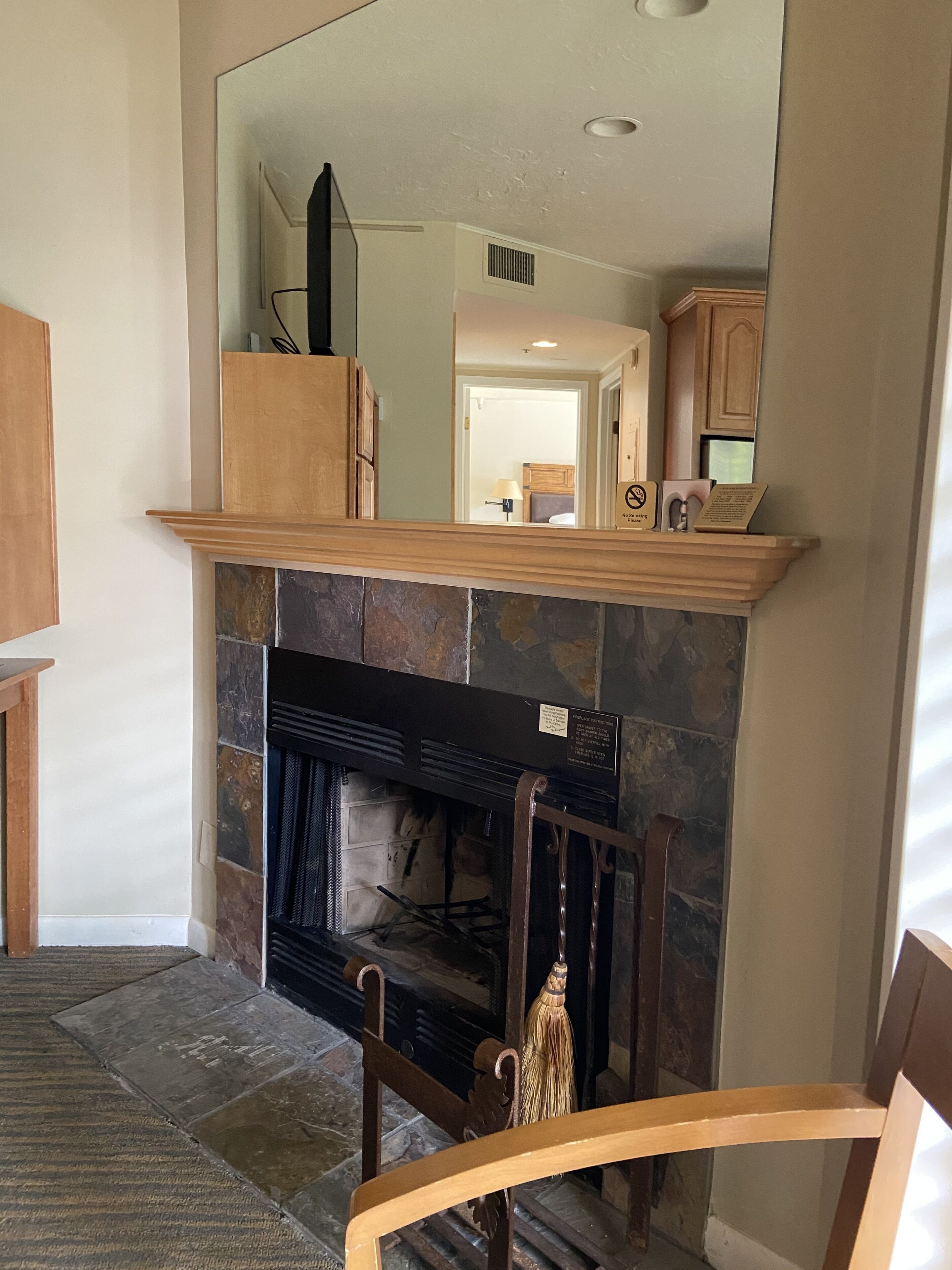 A living room with a stone fireplace, wooden mantel, and a mirror above it.