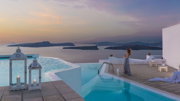 An infinity pool with a view of the sea and islands, white lanterns, and a person in striped pants. - Apanemo Hotel (Santorini)