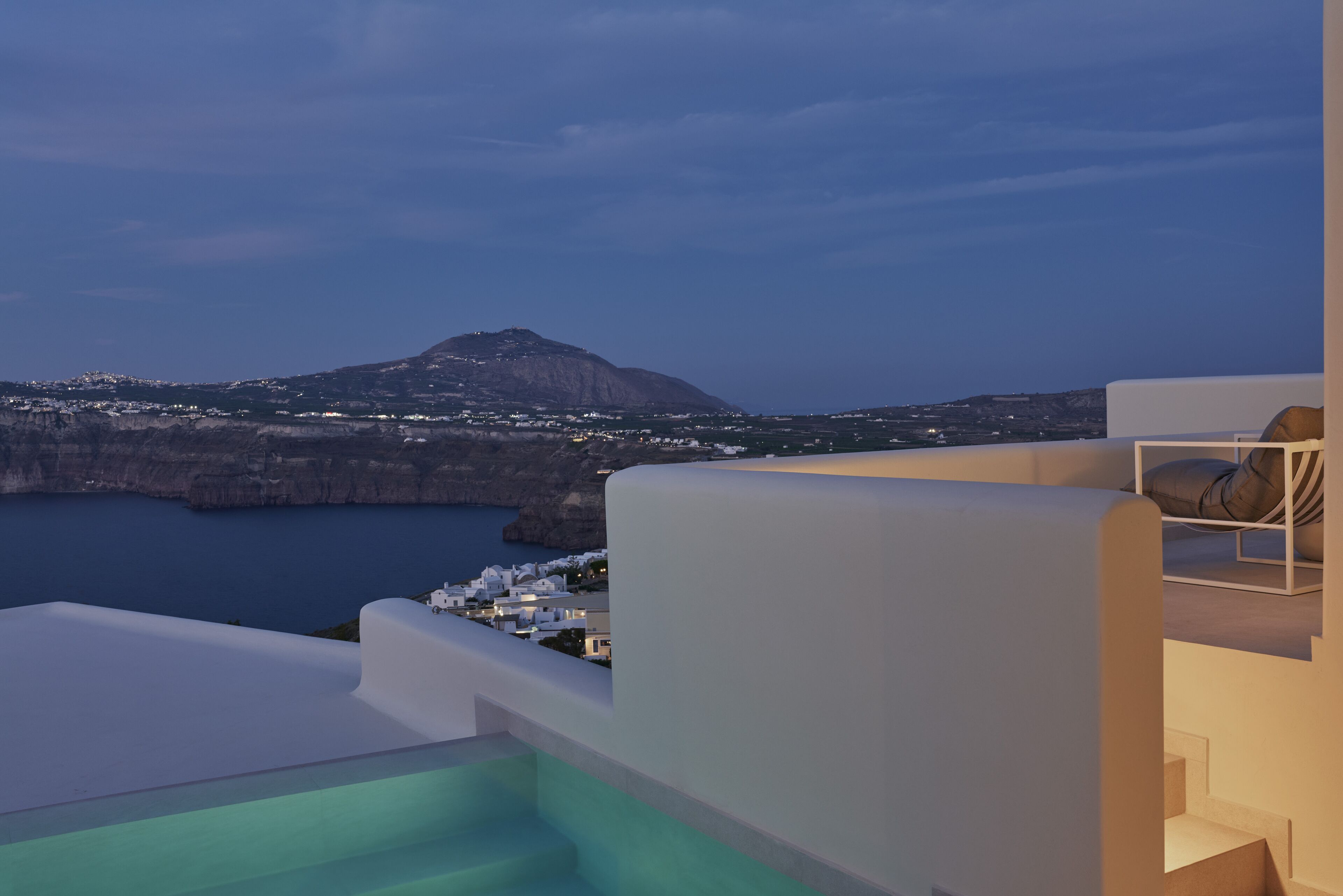 A modern hotel with a pool, white architecture, and a view of the sea and a mountain.