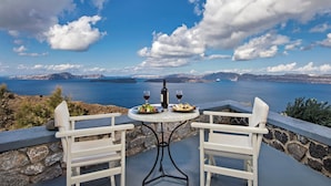 A table with plates of food and wine, overlooking a scenic view of a body of water and mountains. - Apanemo Hotel (Santorini)