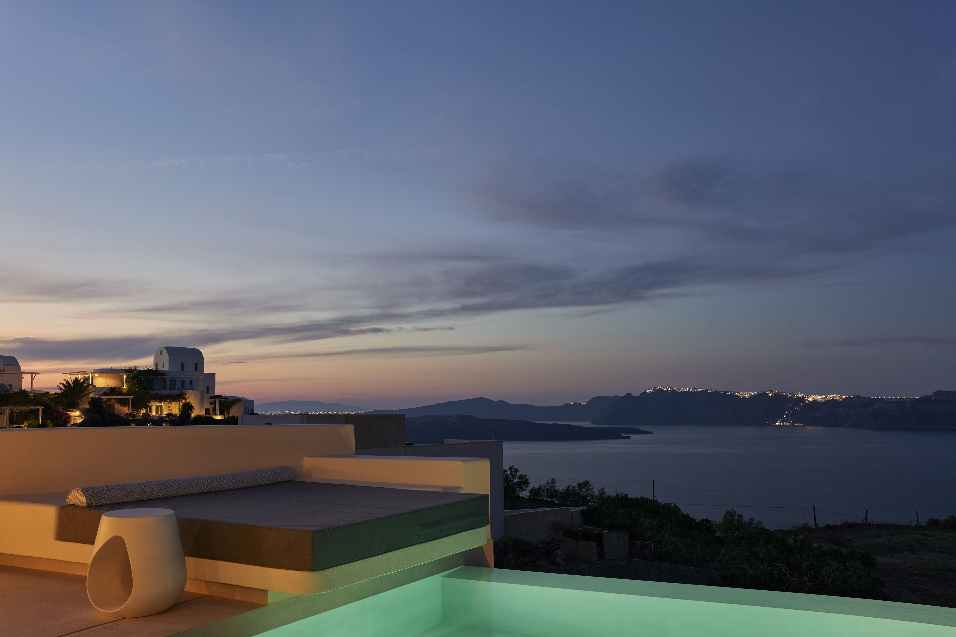 A modern rooftop terrace with a pool, overlooking a coastal landscape and a body of water at dusk.