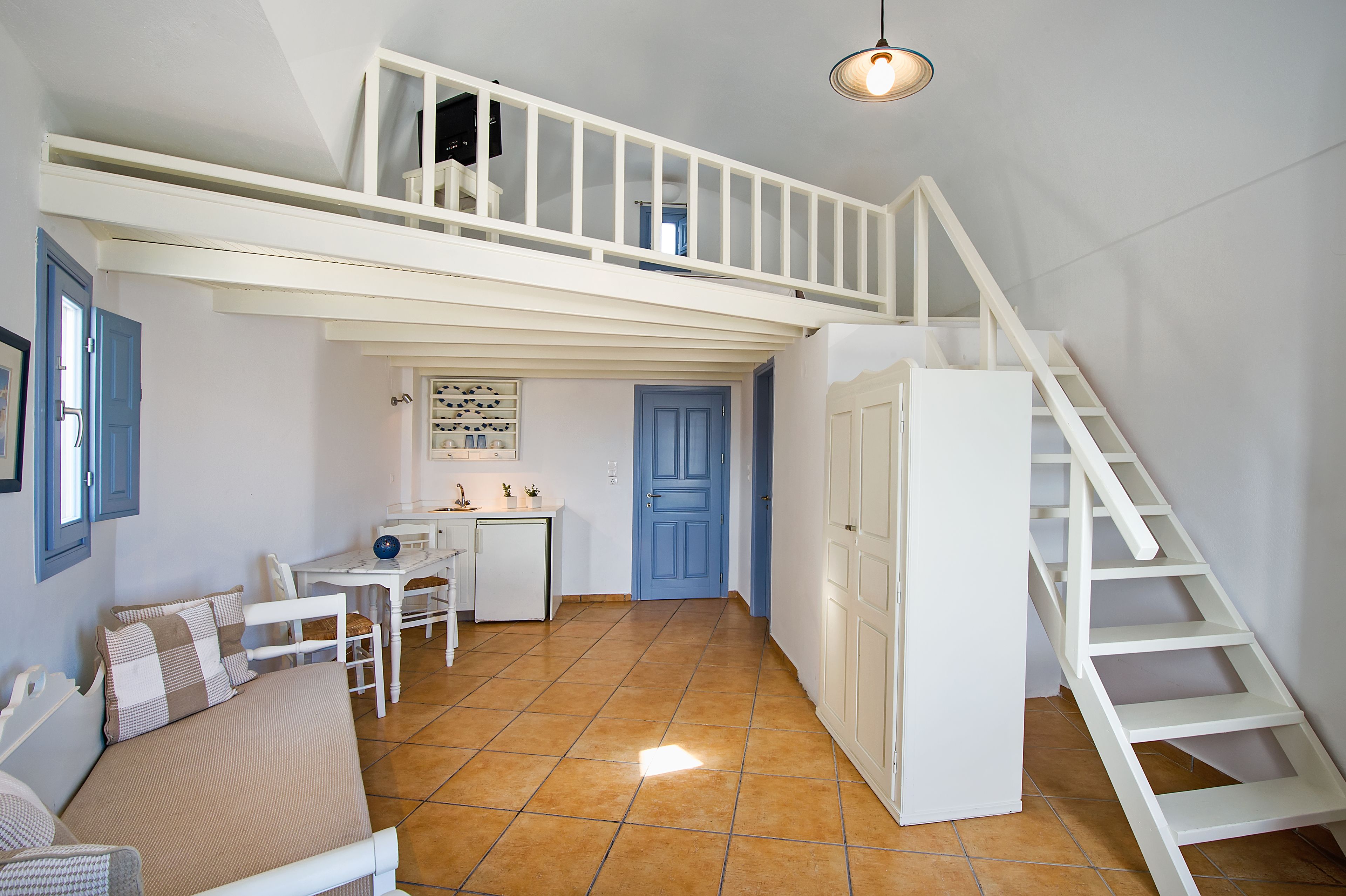 Une chambre spacieuse aménagée en loft, avec une mezzanine, une petite kitchenette et un escalier.