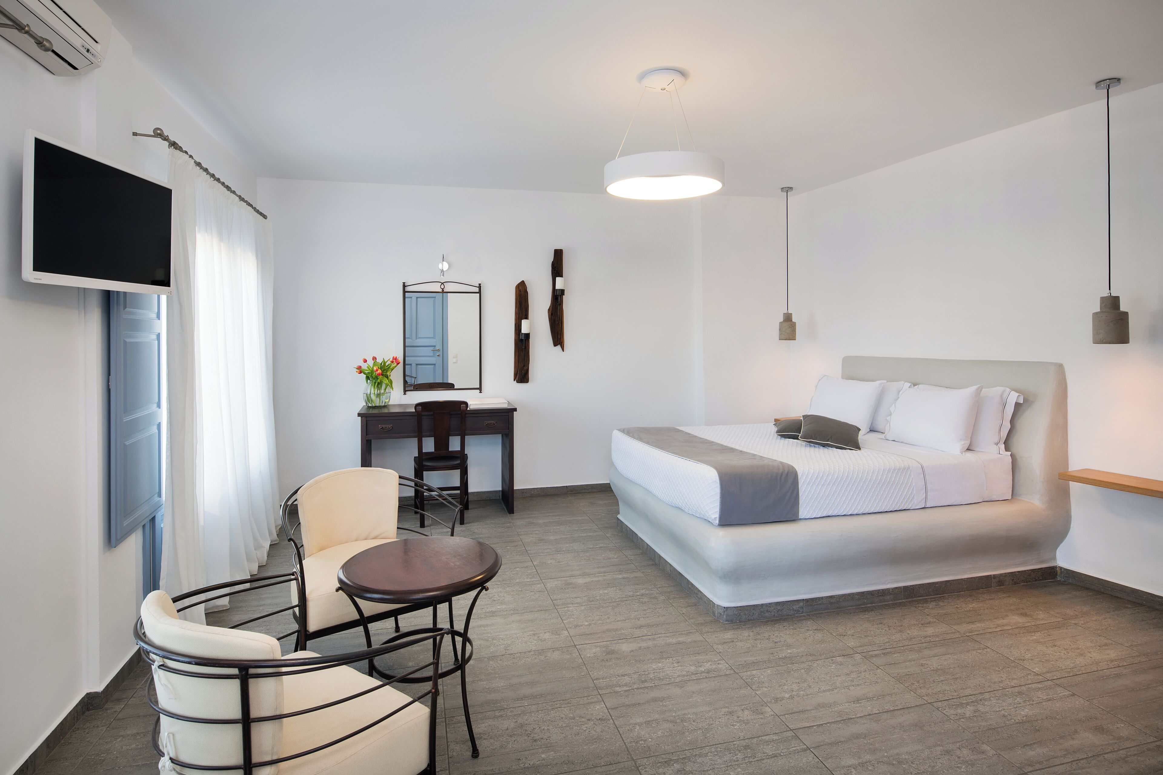 A modern hotel room with a bed, desk, chair, and a flat-screen TV.