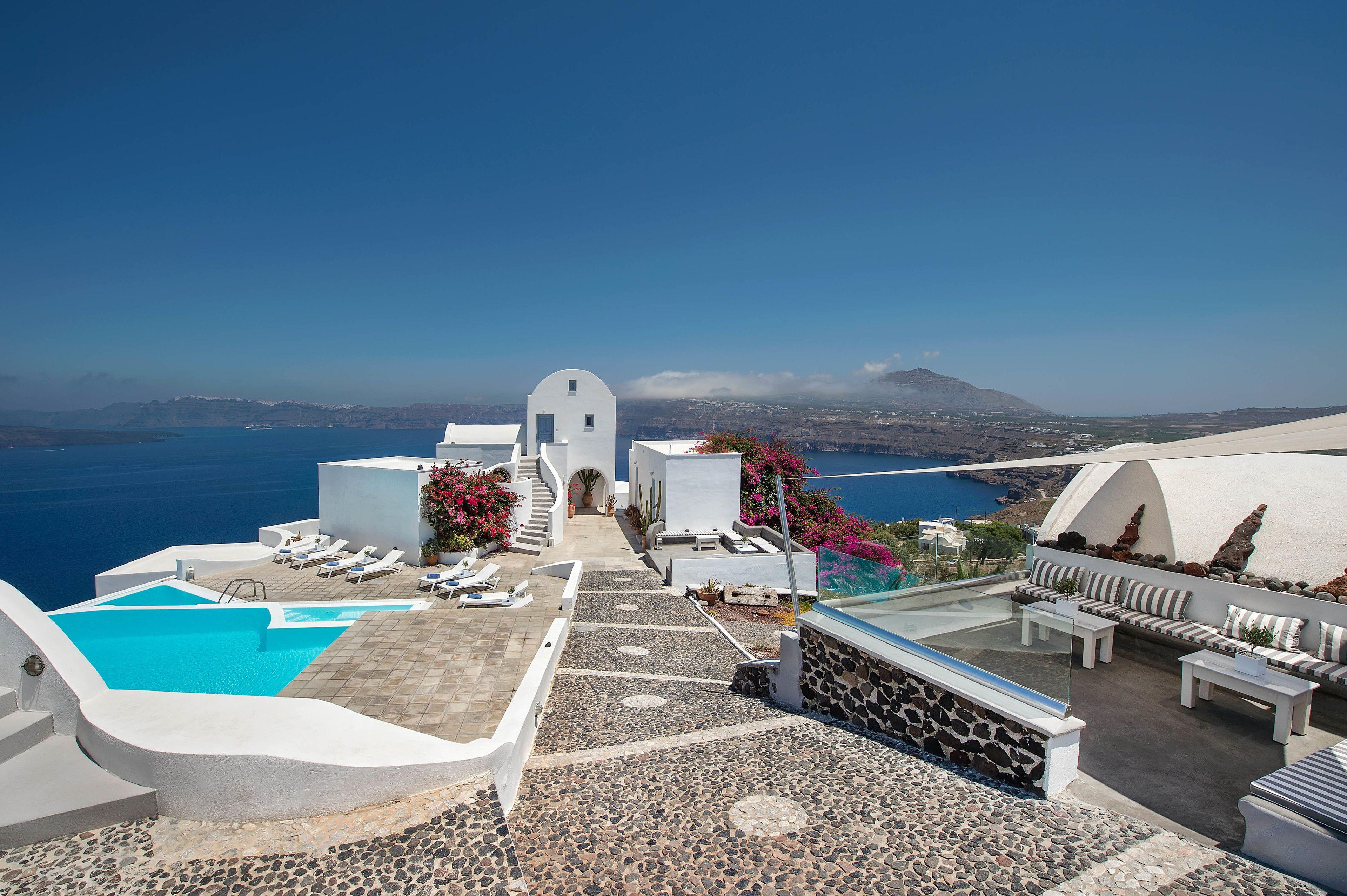 Una terraza en la azotea con piscina, sillones de descanso y vistas al mar y a las montañas.
