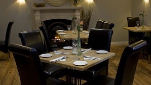 A dining area with a fireplace, a round mirror, and wall-mounted sconces.