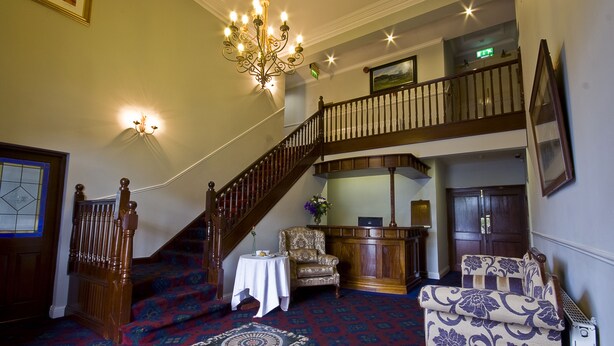 A grand staircase with a chandelier, a patterned carpet, and a seating area with a table and chairs.
