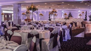 A banquet hall with round tables set for a formal event, featuring white tablecloths and dark chair covers.