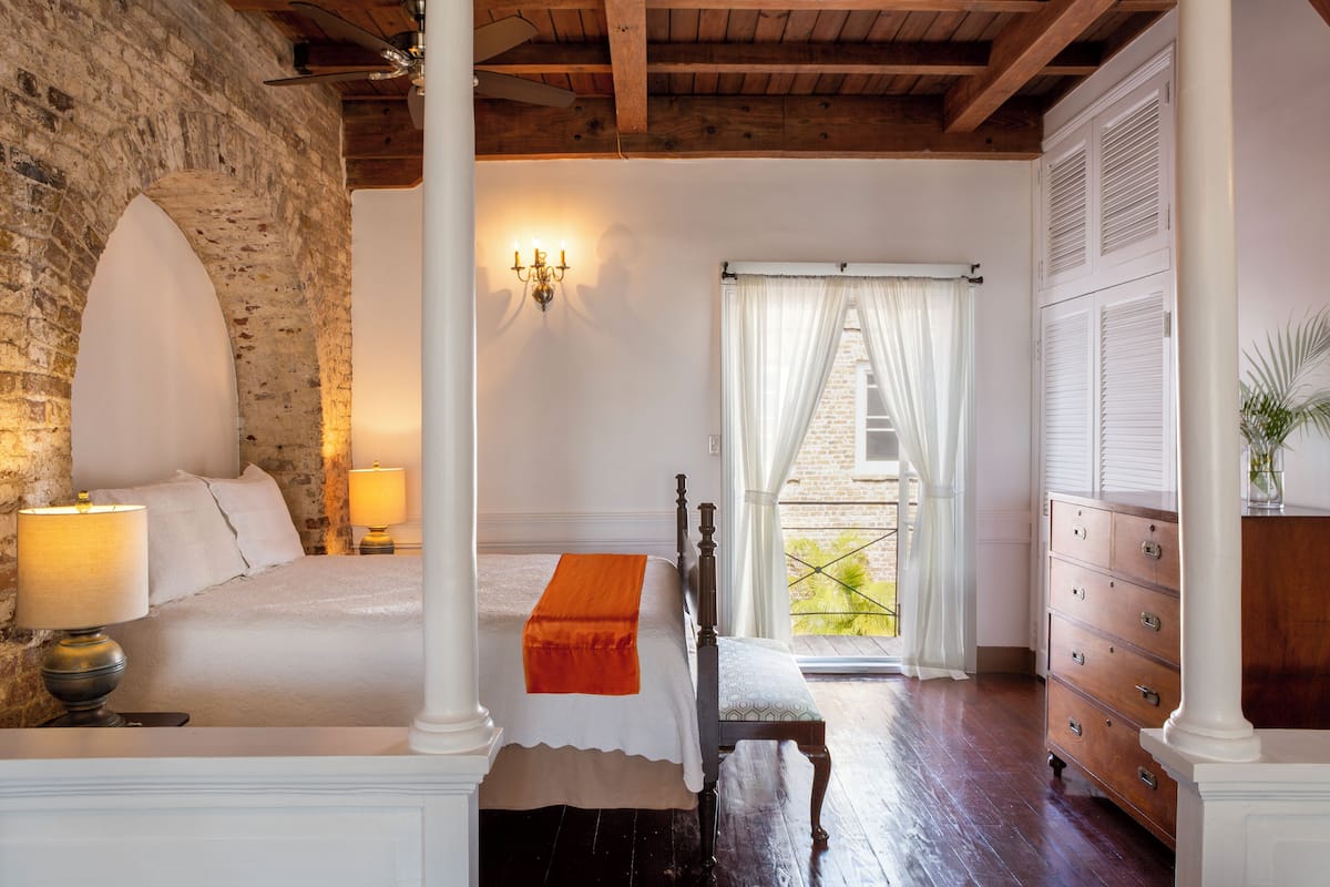A bedroom with a bed, bedside lamps, a bench, a dresser, and a view through a window.