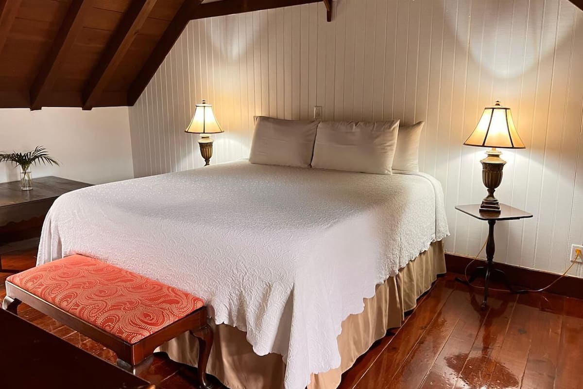 A bedroom with a large bed, two bedside lamps, a wooden bench, and a wooden ceiling.