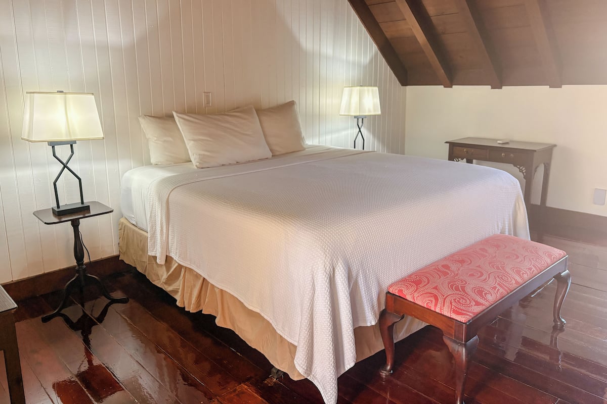 A bedroom with a large bed, two bedside lamps, a wooden bench, and a small table.
