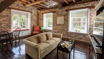 A cozy room with a brick wall, wooden beams, a beige sofa, a dining table with chairs, and a kitchen area.
