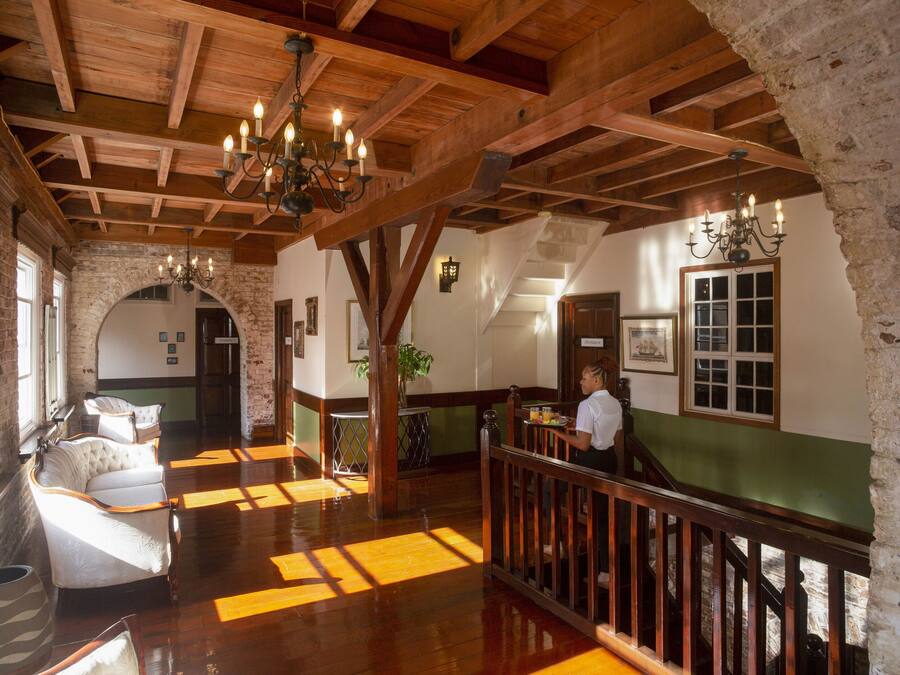 Um hall amplo com vigas de madeira, um candelabro e uma escadaria.