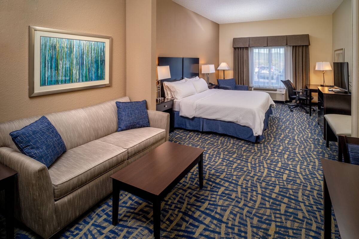 A hotel room with a bed, a sofa, a desk, and a large window.