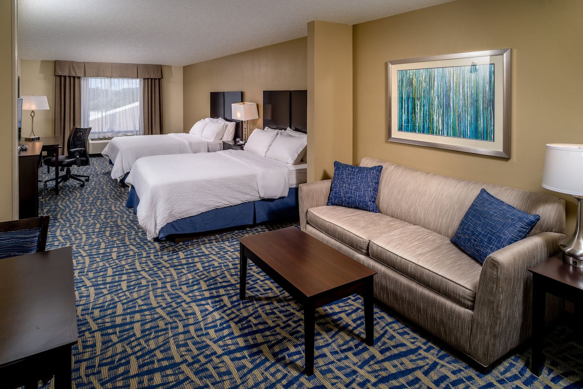 A hotel room with two beds, a sofa, a coffee table, a desk, and a lamp.