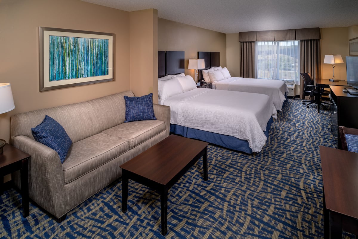 A hotel room with a sofa, two beds, a desk, and a large window.
