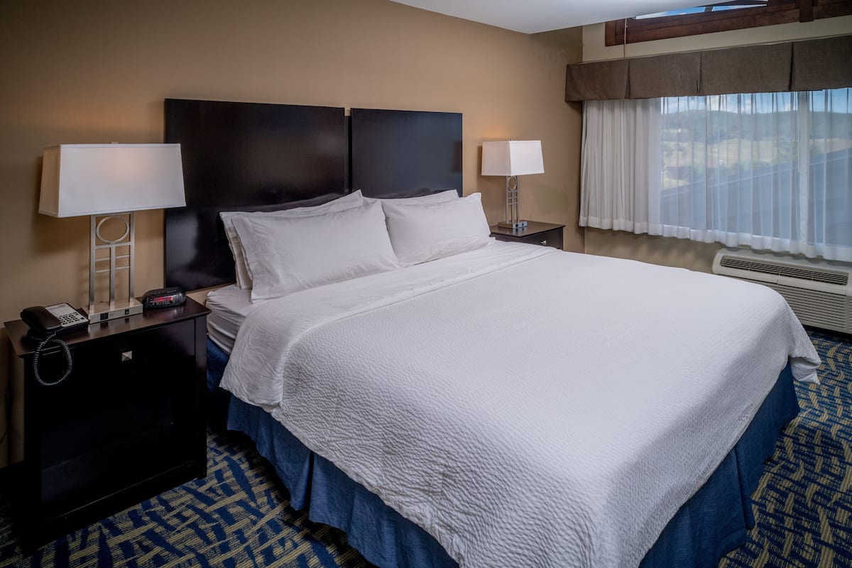 A hotel room with a large bed, two bedside tables with lamps, a telephone, and a window with curtains.