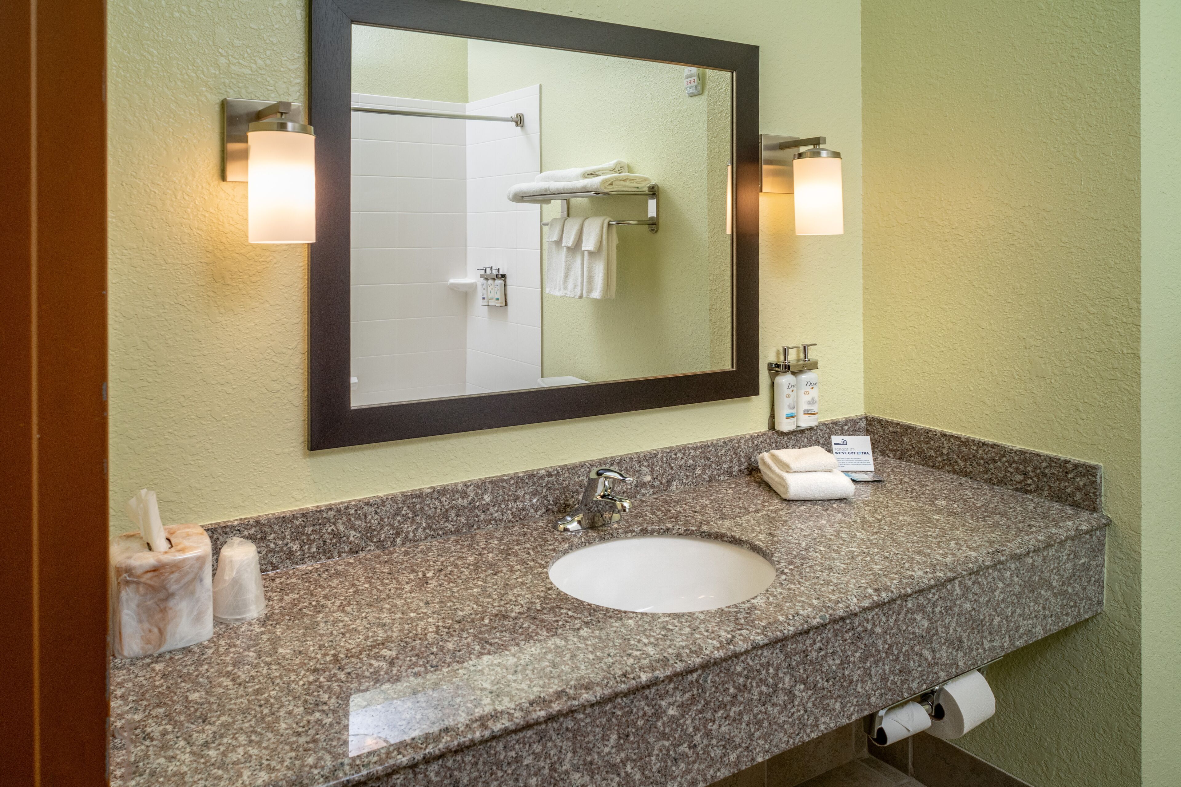 A bathroom with a granite countertop, a sink, a mirror, and two wall-mounted lights.