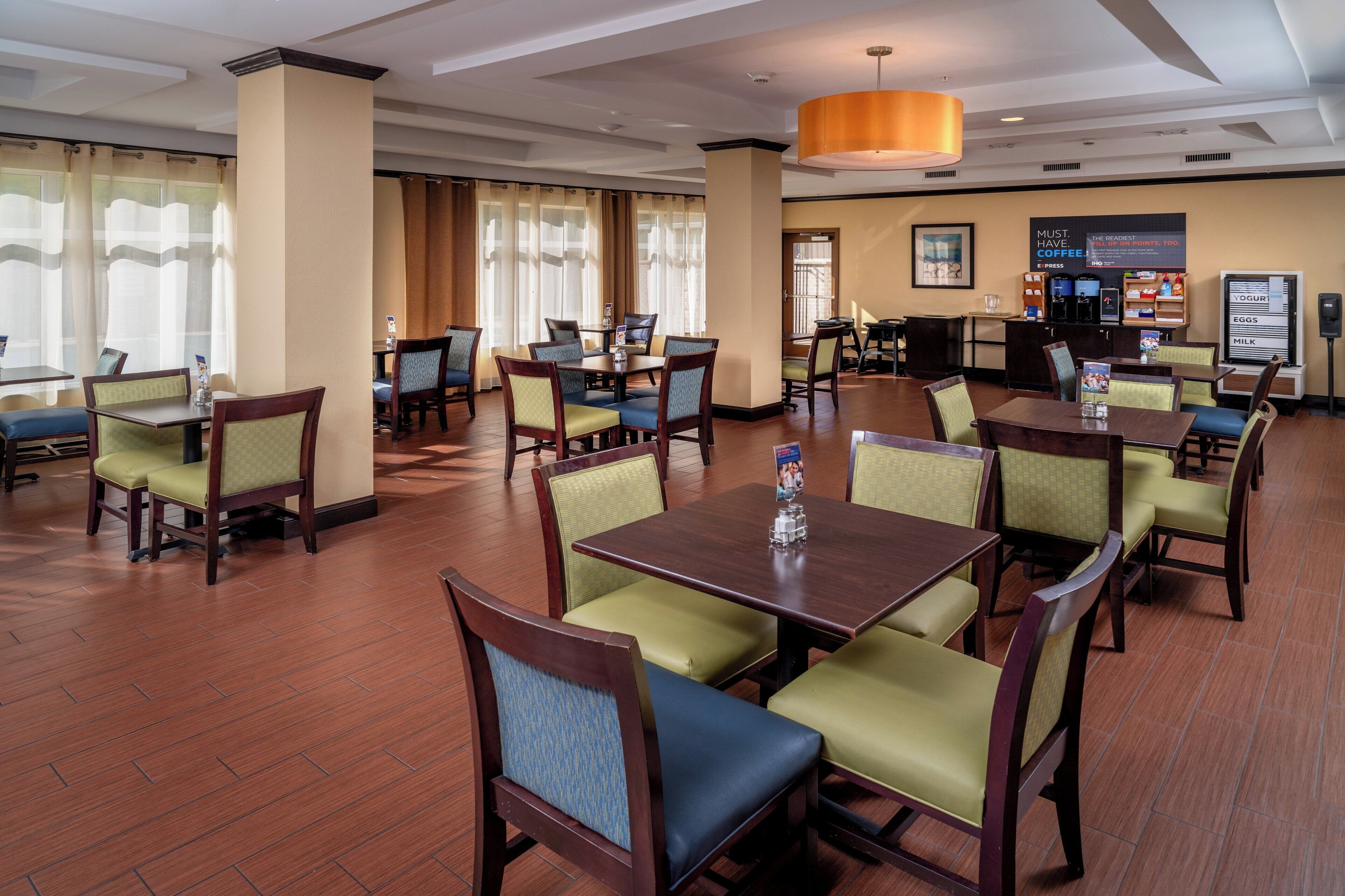 A hotel dining area with multiple tables and chairs, a coffee station, and a menu board.