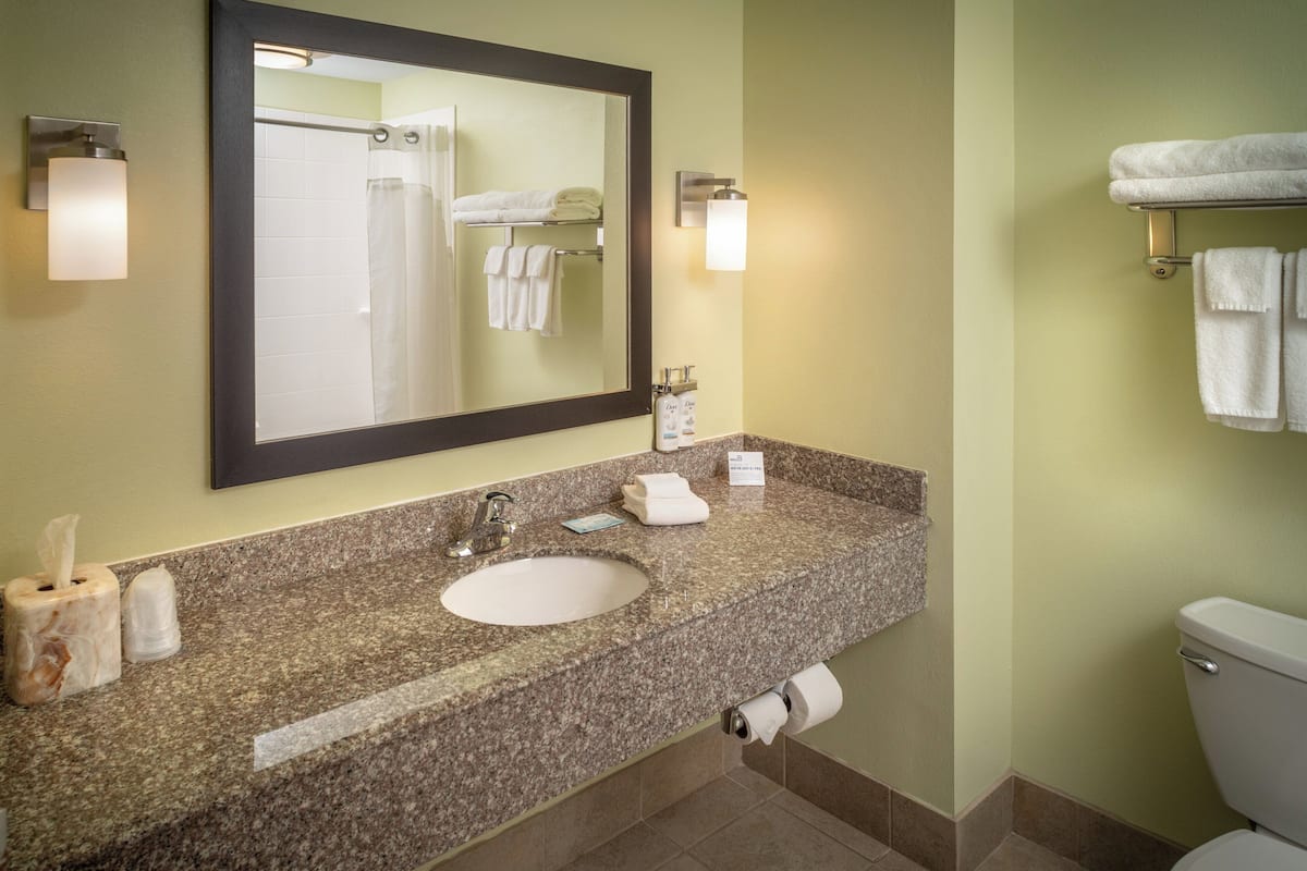 A bathroom with a granite countertop sink, a mirror, a towel rack, and a toilet.