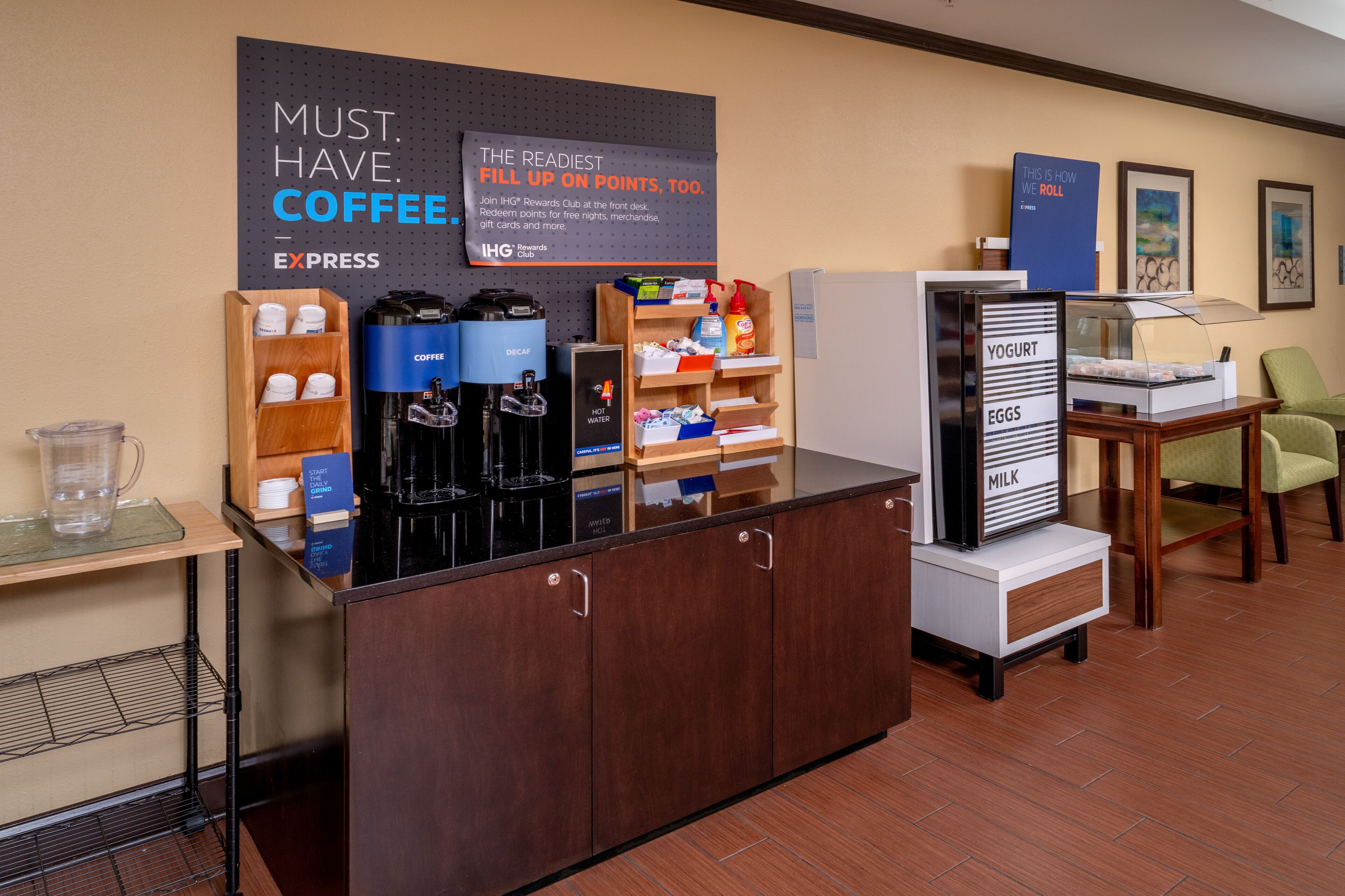 Un espace d’accueil d’hôtel comprenant un coin café, un réfrigérateur contenant des yaourts, des œufs et du lait, ainsi qu’un panneau indiquant l’existence d’un club de fidélité.