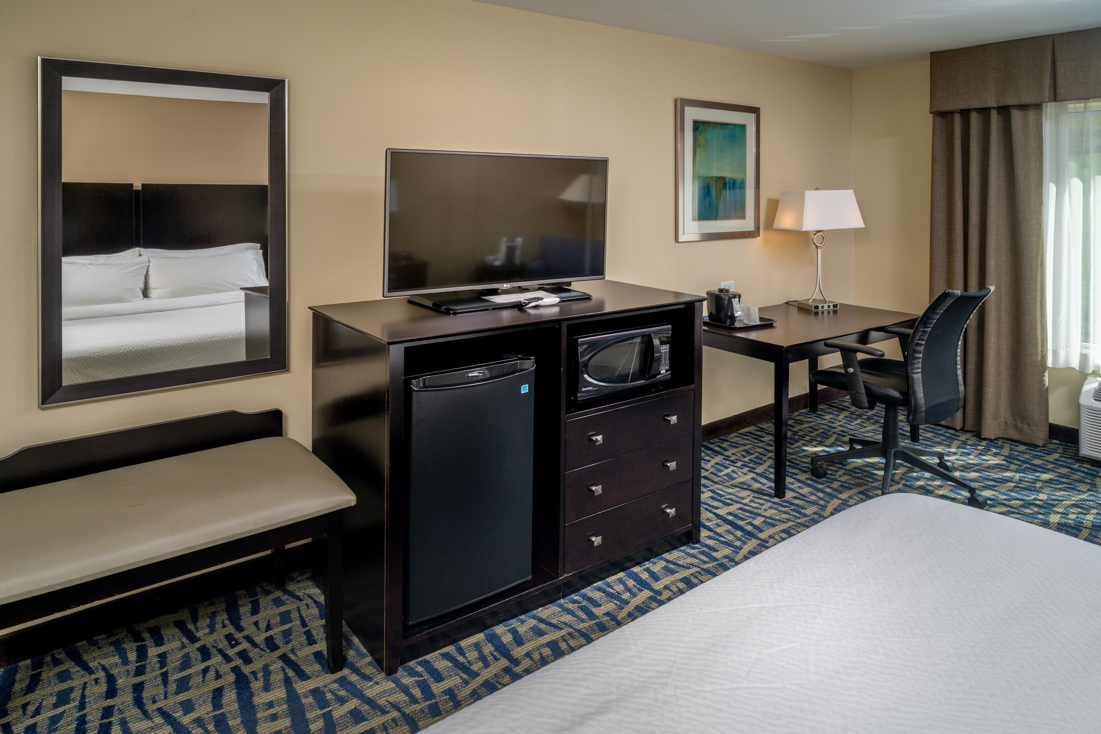 A hotel room with a bed, desk, chair, TV, and a mirror.