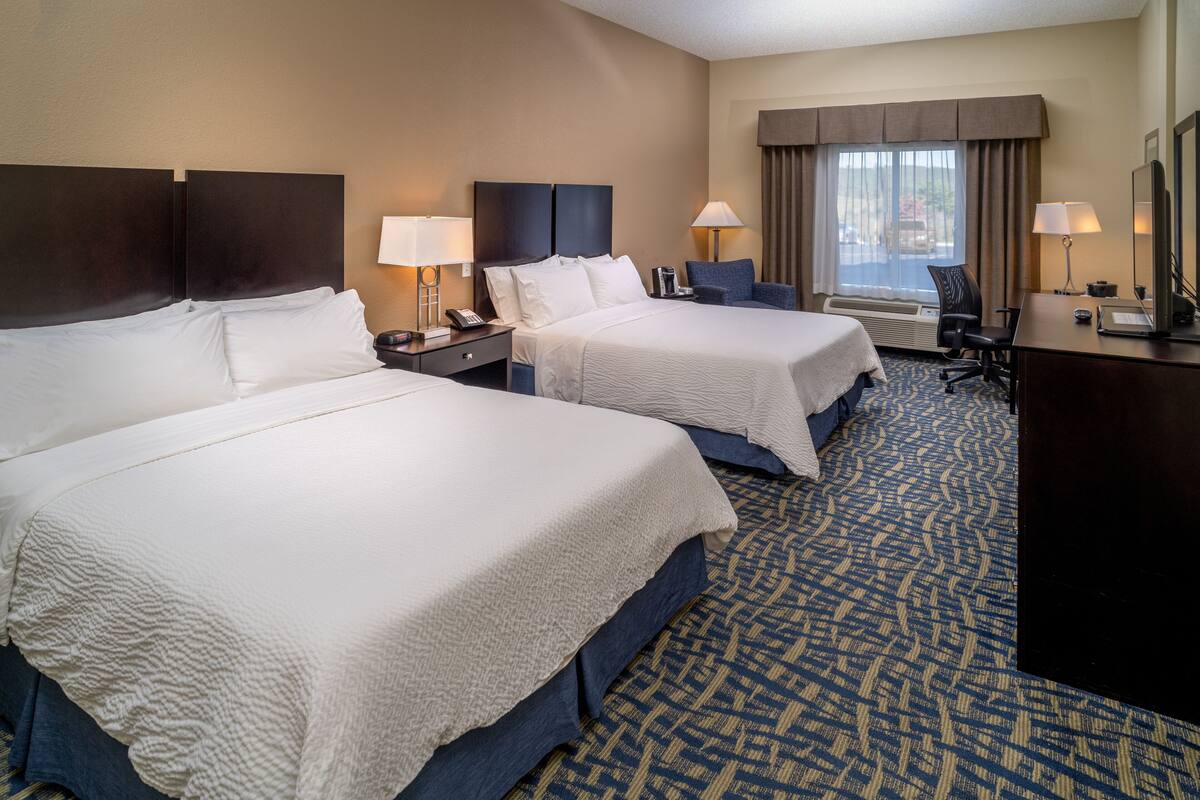 A hotel room with two beds, a desk, a chair, and a large window with curtains.