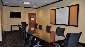 Una sala de conferencias con una larga mesa, seis sillas, un televisor y una pantalla instalada en la pared.