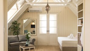 A cozy attic bedroom with a wooden floor, a white bed, a gray sofa, and a small table with a vase. - Landhuis klein Santa Martha (Soto)