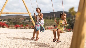 Two children on swings in a garden with a wooden swing set and a gravel ground. - Landhuis klein Santa Martha (Soto)