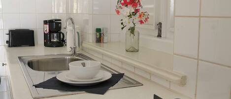 A modern kitchen with white tiles, a gas stove, a coffee maker, a toaster, and a vase with flowers on the counter.