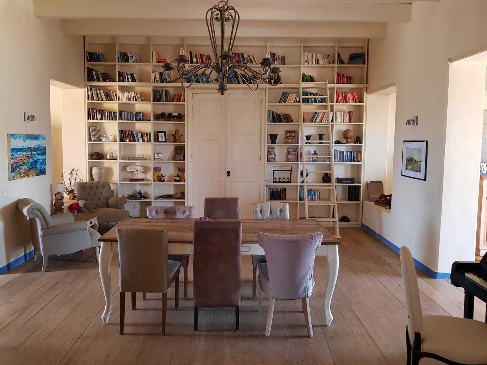 Amplia sala de estar con comedor, con una gran estantería llena de libros y objetos decorativos, un candelabro y un piano.
