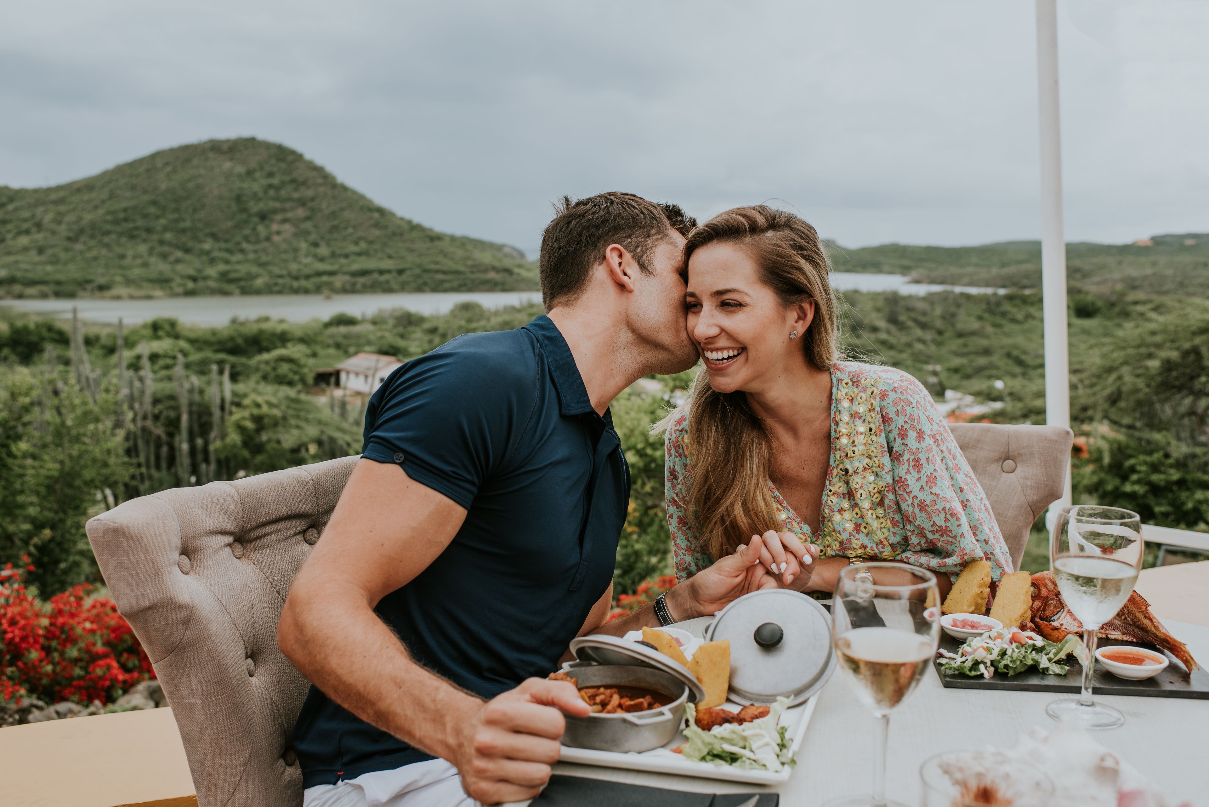 A couple dining outdoors with a scenic view of a lake and hills.