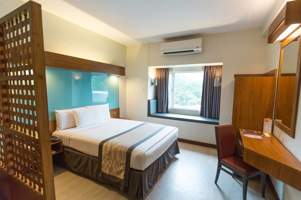 Une chambre d’hôtel comprenant un lit, un bureau, une chaise, une fenêtre avec des rideaux, un appareil de climatisation et une cloison en bois.