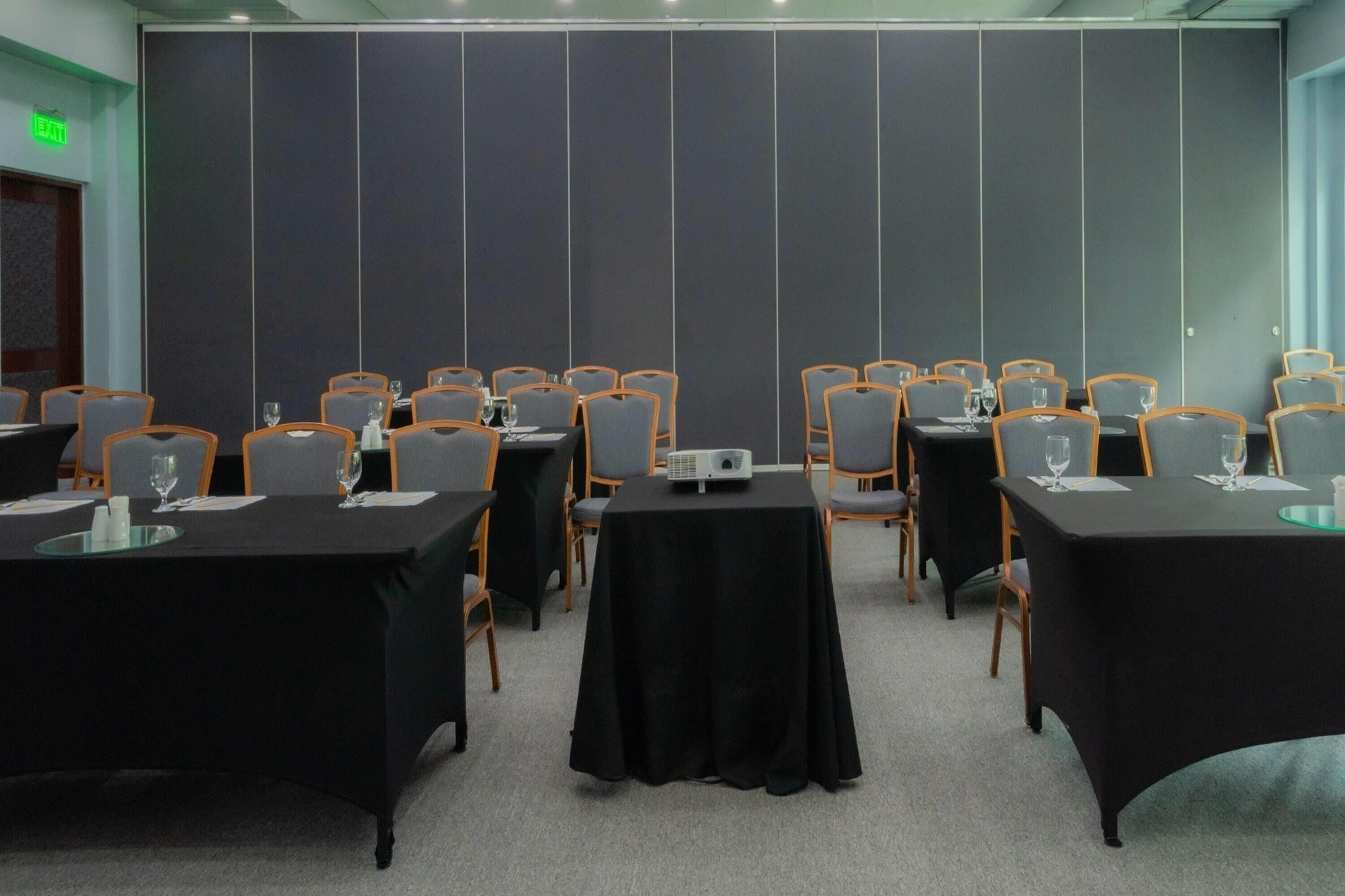 Un salón de conferencias con varias mesas, sillas y un proyector.