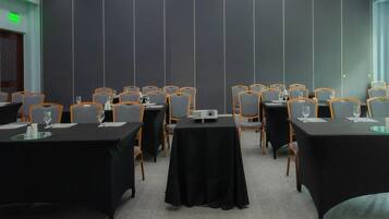 Un salón de conferencias con varias mesas, sillas y un proyector.
