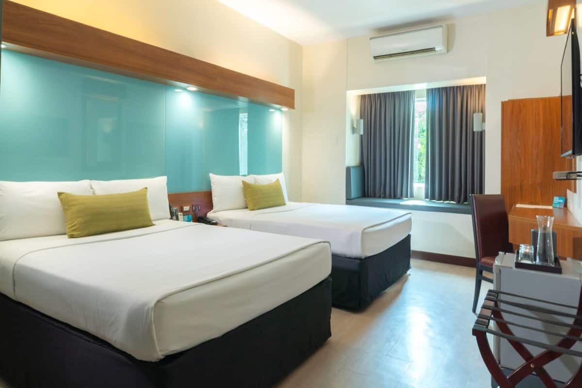Une chambre d’hôtel avec deux lits, un bureau, une chaise et un appareil de climatisation.