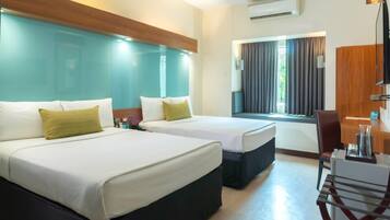 Quarto de hotel com duas camas, uma escrivaninha, uma cadeira e um ar condicionado.