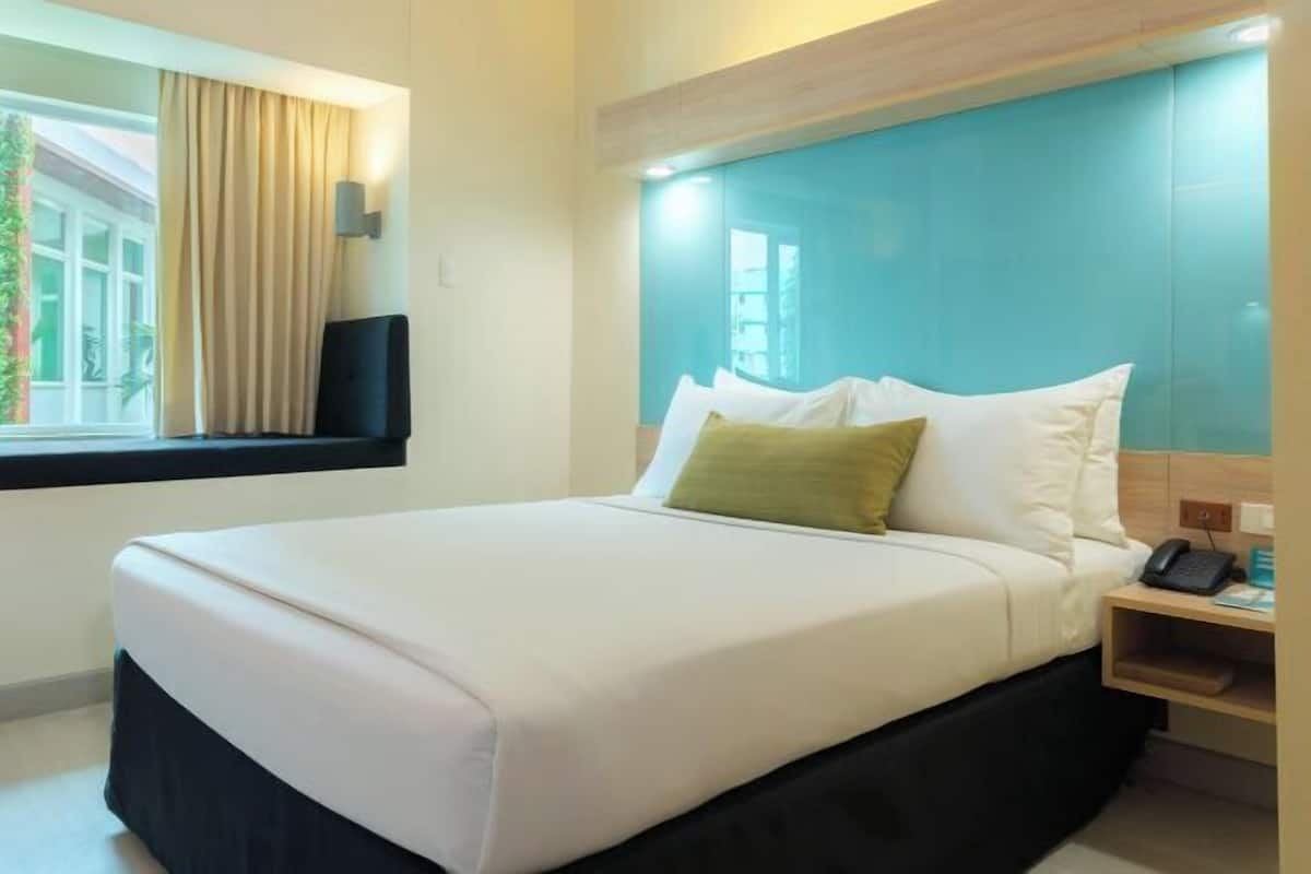 Une chambre d’hôtel avec un lit, une table de chevet, une fenêtre avec des rideaux et une vue sur la verdure.