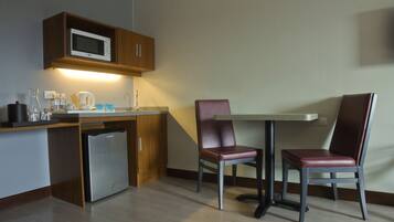 A compact kitchen with a microwave, refrigerator, and a small coffee maker. There are two chairs and a table, suggesting a small dining area.
