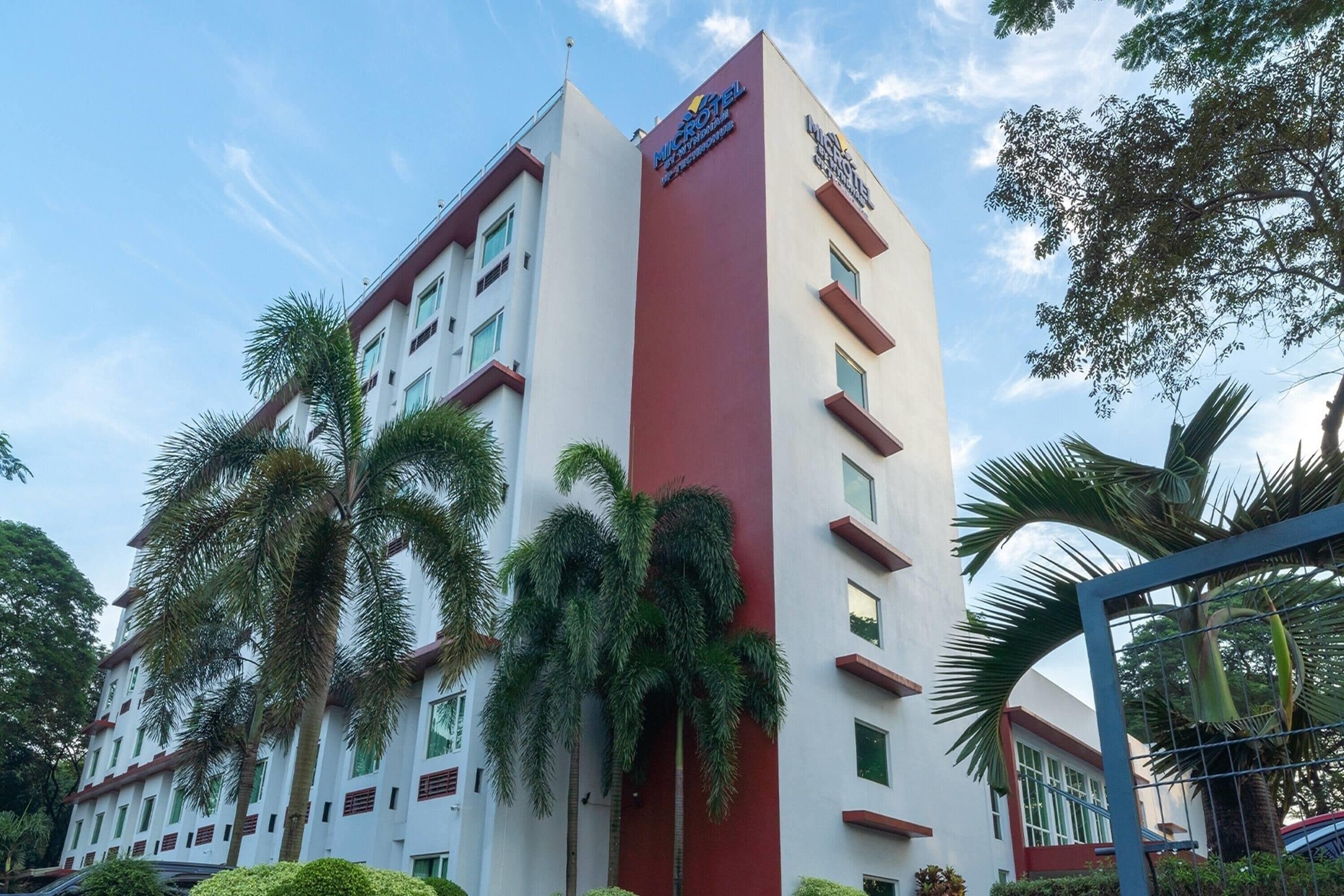 A multi-story hotel with a prominent red and white facade, palm trees, and a clear sky.