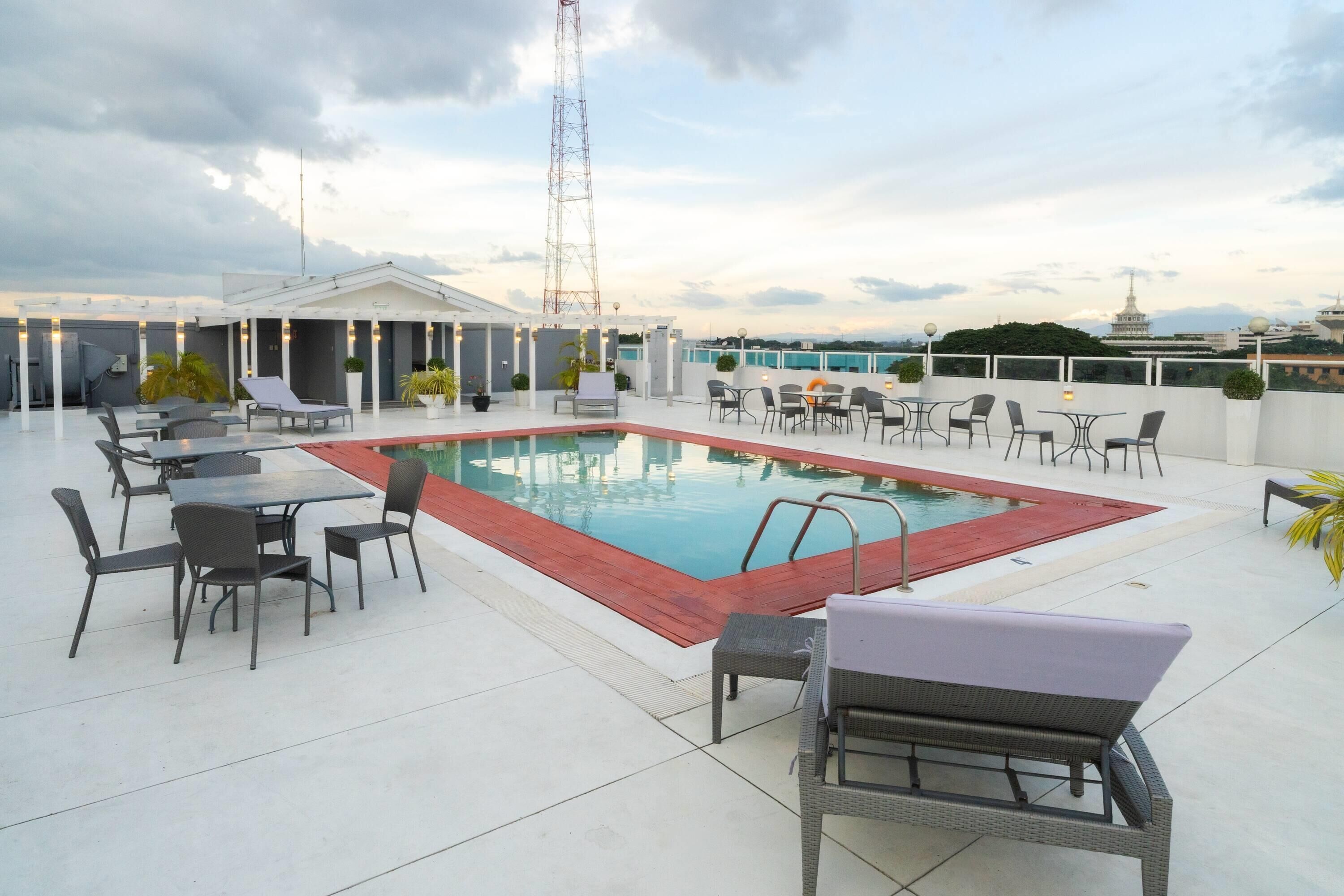 A rooftop pool area with lounge chairs, tables, and a view of the city skyline.