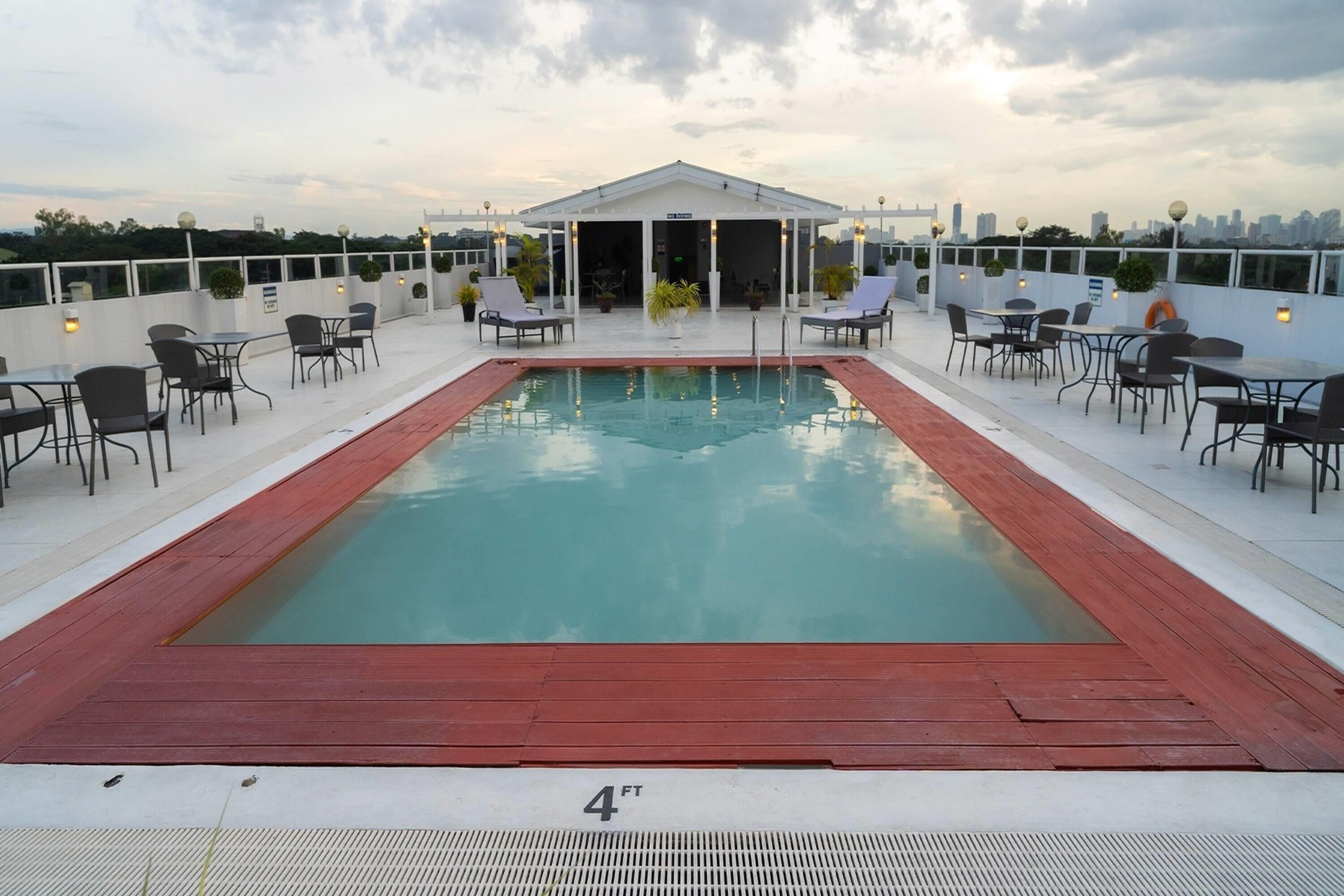 A rooftop pool with a wooden deck, lounge chairs, and tables.