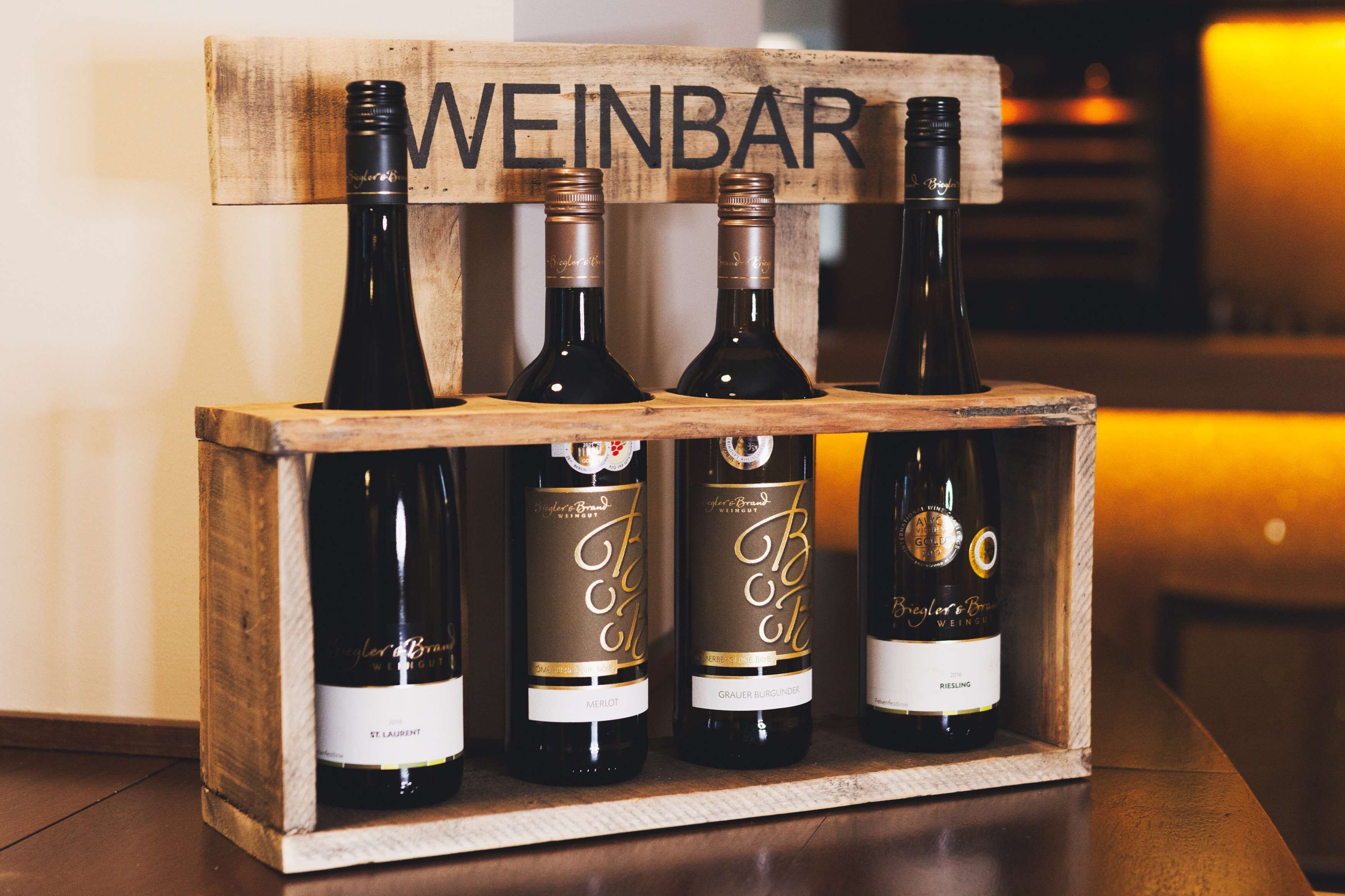 A wooden wine rack with four bottles of wine labeled 'Weinbar'.