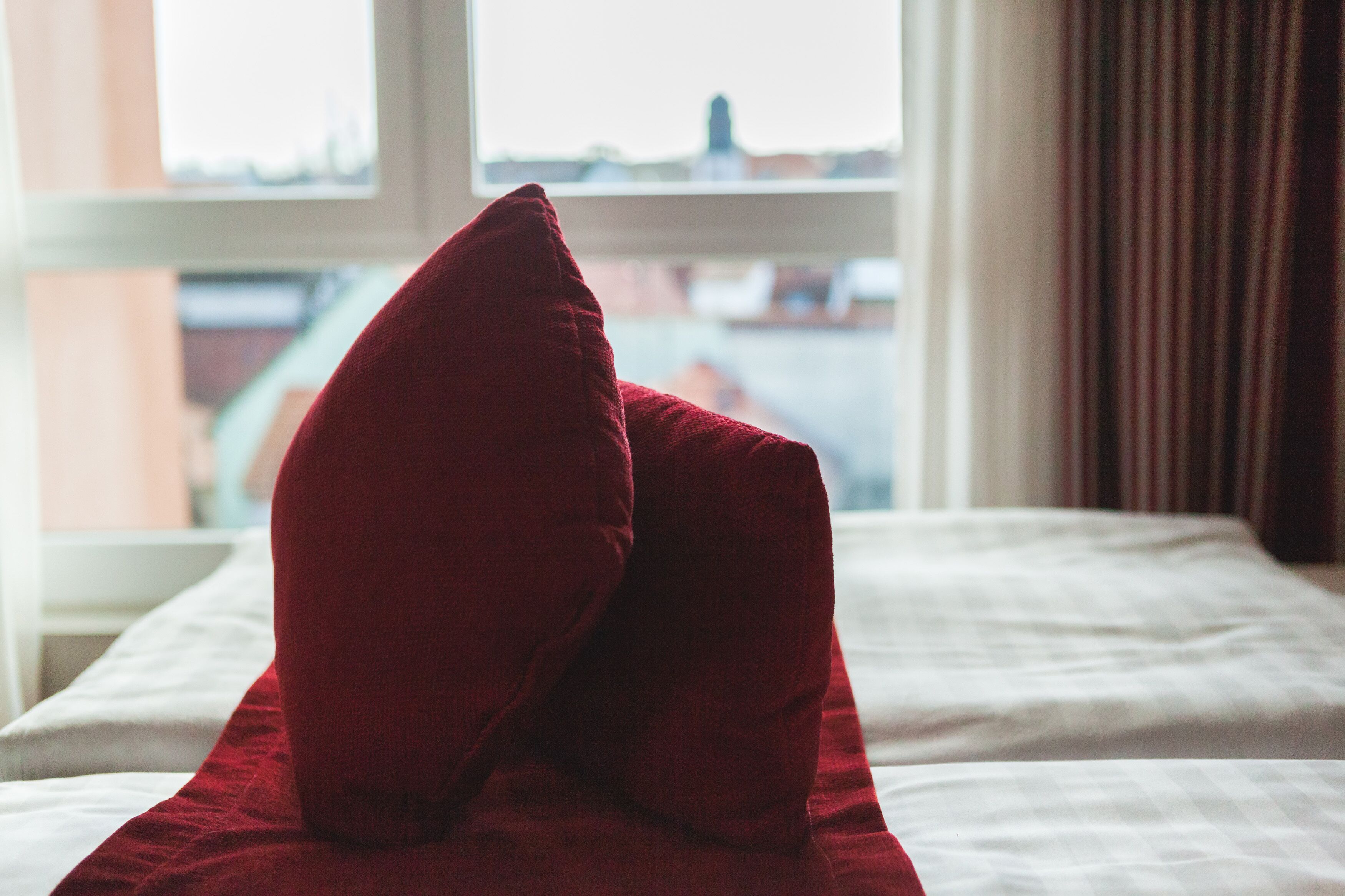 A bed with a red pillow and a white bedspread.